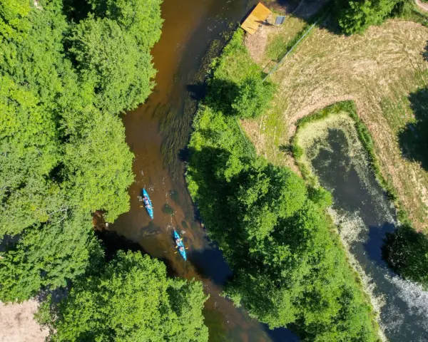 Spływ kajakowy rzeką to jedna z pięknych kociewie atrakcji. Dwie kajaki płyną wśród zielonych drzew.