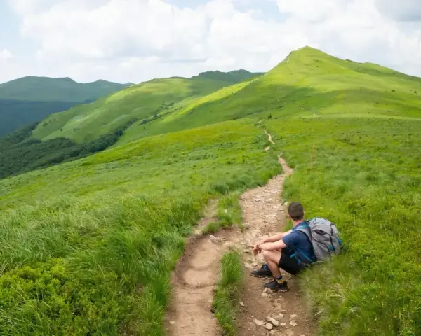 Wędrowiec odpoczywa na szlaku, podziwiając zielone połoniny. Idealny widok na Bieszczady w 3 dni co zobaczyć.