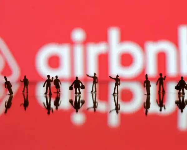 Małe figurki ludzi na tle logo Airbnb. Zastanawiasz się airbnb co to? To platforma do rezerwacji noclegów.