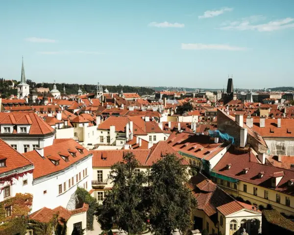 Widok na dachy Pragi, idealne miejsce na tani city break. W oddali wieże i kopuły.