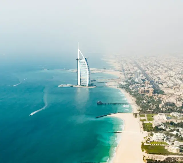 Widok z lotu ptaka na Dubaj: luksusowy hotel w kształcie żagla, piaszczysta plaża i turkusowe morze.