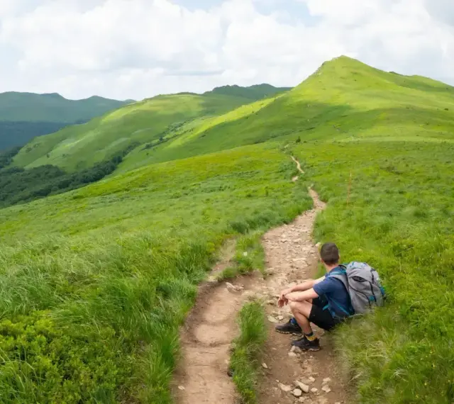 Wędrowiec odpoczywa na szlaku, podziwiając zielone połoniny. Idealny widok na Bieszczady w 3 dni co zobaczyć.