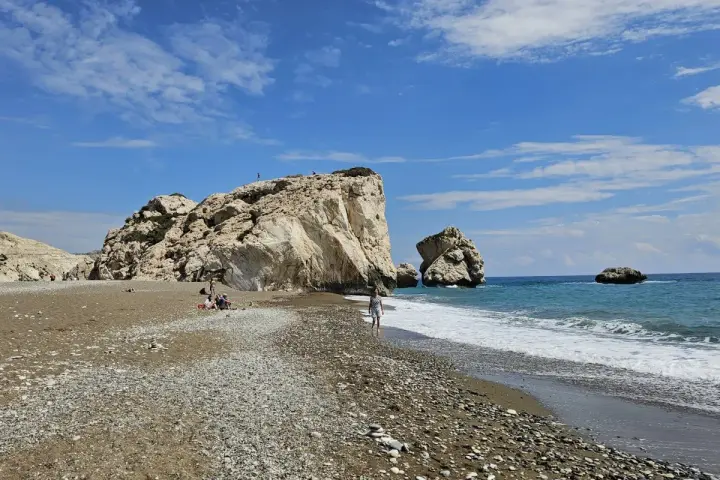 Skała Afrodyty na Cyprze, z turkusowym morzem i kamienistą plażą. Ludzie odpoczywają i spacerują.