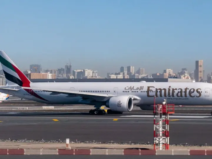 Samolot Emirates na płycie lotniska, w tle panorama Dubaju. Zastanawiasz się, ile się leci do Dubaju?