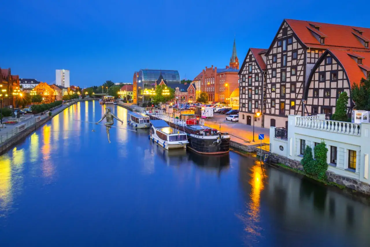 Bydgoszcz nocą: rzeka Brda, łodzie, zabytkowe kamienice i rzeźba na linie. Nietypowe atrakcje Bydgoszcz zachwycają o zmierzchu.