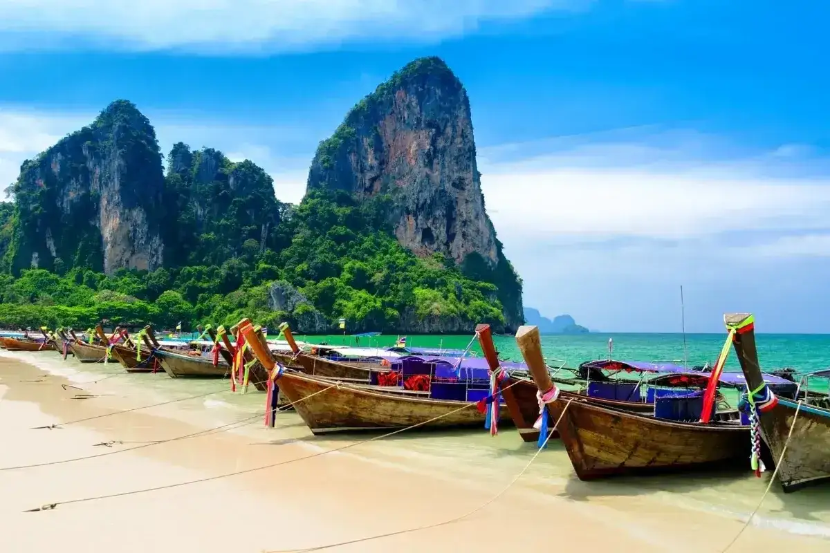 Tajlandia najpiękniejsze miejsca: łodzie na plaży Railay Beach, Krabi, z wapiennymi klifami w tle.