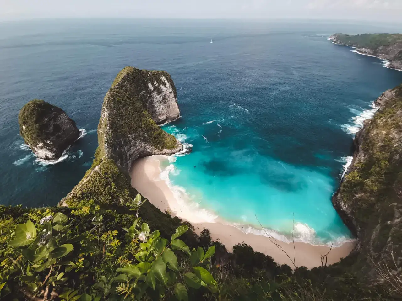 Widok na turkusowe plaże na Bali, z klifami porośniętymi zielenią i skalnymi formacjami w oceanie.