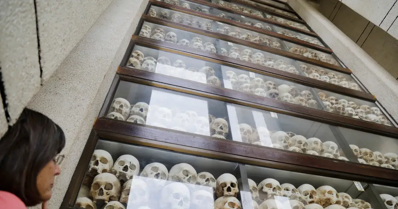 Ludzie oglądają ludzkie czaszki w szklanych gablotach, przypominające o tragicznych wydarzeniach w polach śmierci Kambodży.