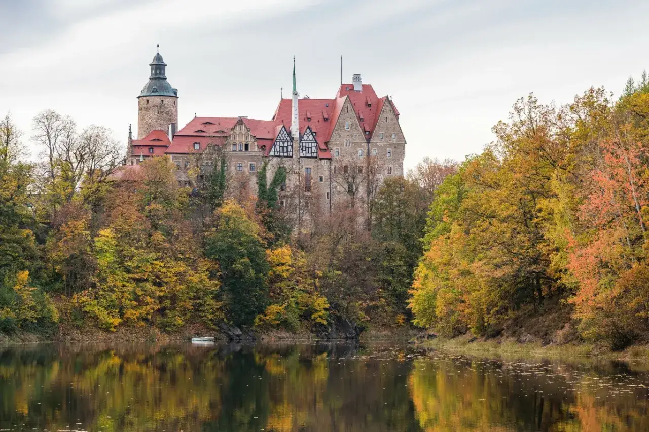 Zamek Kliczków w jesiennej odsłonie, idealne miejsce na jednodniowy wypad w Polsce. Otoczony kolorowymi drzewami, odbija się w spokojnej tafli wody.