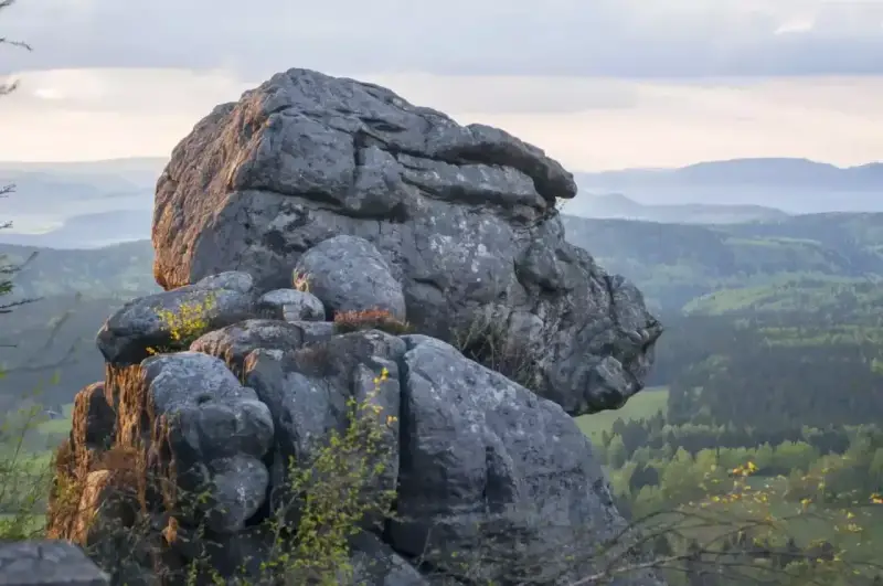 Skaliste formacje na tle zielonych gór w Czechach. Słońce oświetla skały, tworząc ciekawe cienie.